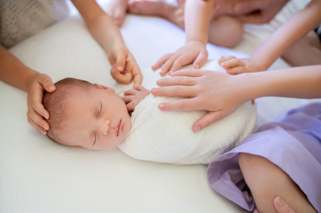 siblings hands on newborn baby 